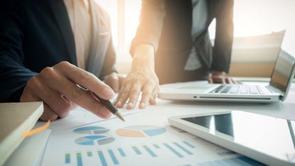 two people looking at charts and laptops