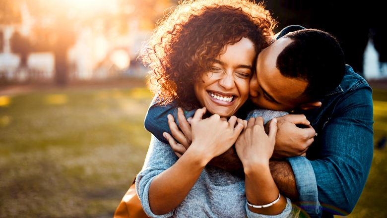 woman smiling with man hugging her in park