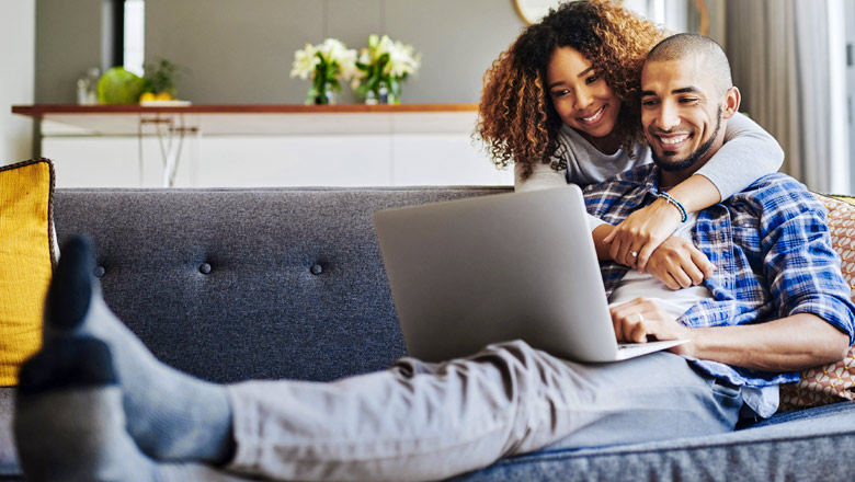 Couple sitting on a couch looking at a laptop