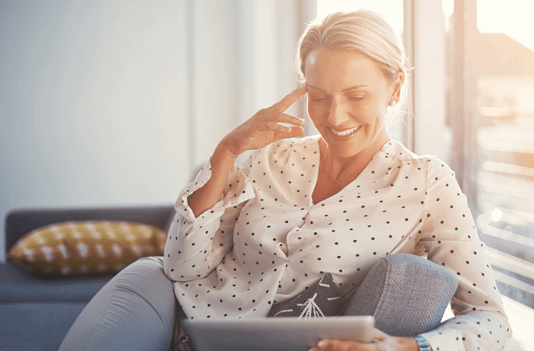 woman smiling looking at tablet on a sofa