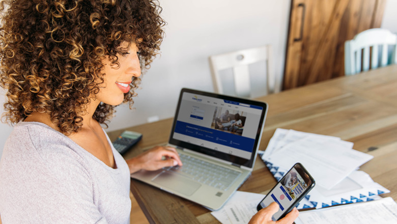 woman at table with bills using computer and phone