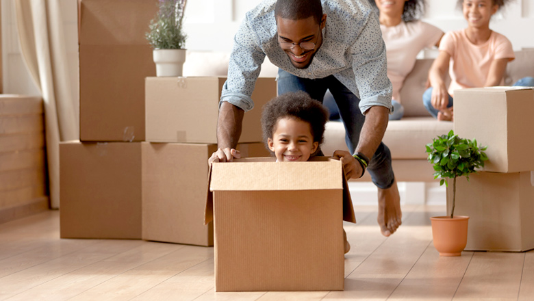 dad pushing young son in a box at new home